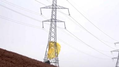 A large electricity pylon with yellow material resembling a parachute wrapped around the bottom of it.