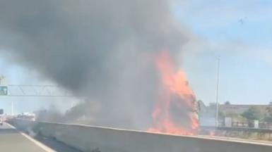 Flames and thick smoke rise from a lorry fire at the side of a major road.