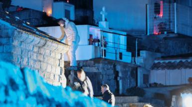 Forensic specialists work in a darkened cemetery