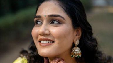 A closeup photo of Twisha Sharma - she's wearing danglers and a green bindi 