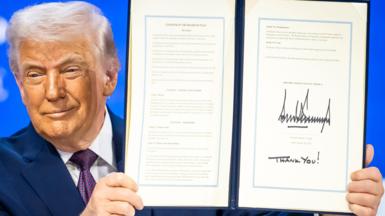 A smiling Donald Trump holds a signed founding charter at the 'Board of Peace' meeting during the 56th annual meeting of the World Economic Forum in Davos. His signature is at the bottom of the document and the words "Thank You!"