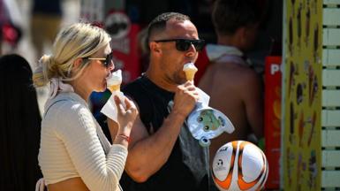 A man and woman wearing sunglasses each eat an ice cream at Bournemouth Beach. 