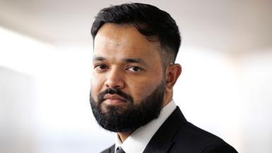 Azeem Rafiq, a bearded man wearing a white shirt and black blazer. The background is plain light.