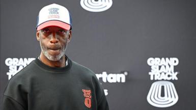 Michael Johnson looking pensive as he stands in front of a black board bearing the Grand Slam Track name and logo