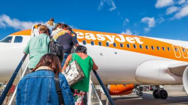 People climb the stairs onto an easyJet orange and white plane.