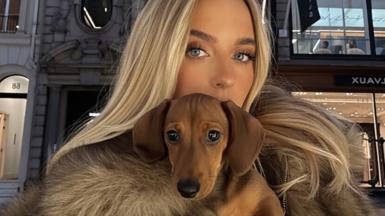 A woman with blond hair holding a Dachshund dog - the dog is AI generated.