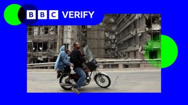 Man, woman and child on a motorbike passing in front of destroyed facade of the Gandhi hospital in Tehran