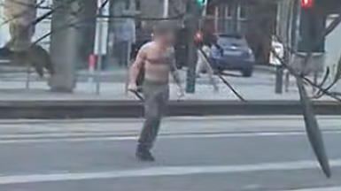 A bare chested man carrying what appears to be a large knife on a street