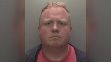 Robert Bush with short, light brown hair is shown in a straight‑on mugshot photograph. He has a neutral expression and is wearing a dark jacket over a red shirt. The background is plain and grey, and a Humberside Police badge watermark appears in the upper right corner of the image.