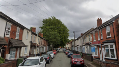 A view of a narrow street of terraced houses in Wolverhampton, with cars parked along both sides.