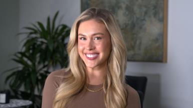 A girl with long blonde hair smiling in a office setting at her desk