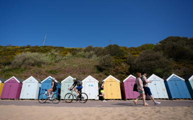 People make their way past beach huts on Bournemouth beach in Dorset.