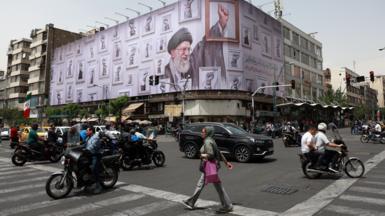 Iranians walk and drive in cars and on motorbikes near a huge poster of late Iranian supreme leader Ayatollah Ali Khamenei in a street in Tehran,