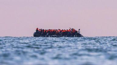 A side view of a small rubber boat filled with people wearing life jackets crosses the English Channel towards the UK.