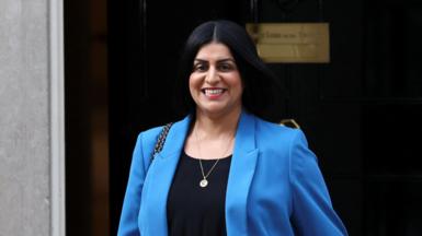 Shabana Mahmood, walking down Downing Street, smiling and wearing a blue blazer.