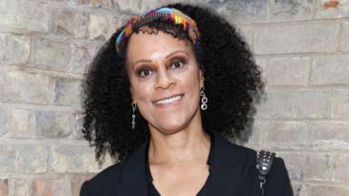 Bernardine Evaristo, wearing a black top, a headband and dangly earrings.