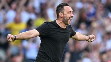 Roberto de Zerbi celebrates with a broad smile and arms outstretched as he runs on to the pitch in a black T-shirt