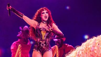 Chappell Roan holding a microphone above her head while performing on stage wearing a corset 