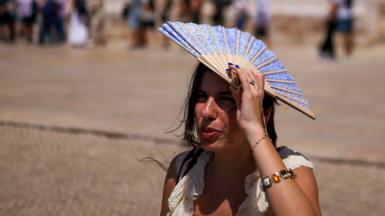 A woman shades her head with a fan in front of Jeronimos Monastery in Belem, Portugal