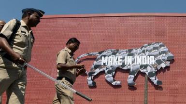 Indian policemen walk past a logo at the venue for the 'Make in India' showcase week in Mumbai on February 11, 2016