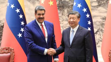 Venezuelan president Nicolás Maduro (L) and Chinese president Xi Jinping shake hands and smile in front of Venezuelan and Chinese flags at the palace in Beijing in 2023.