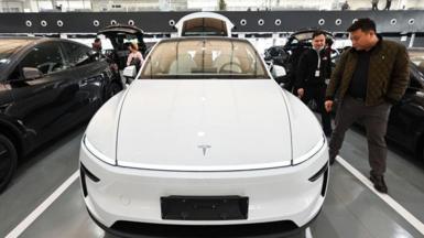 People looking at a white Tesla car in a showroom in Beijing