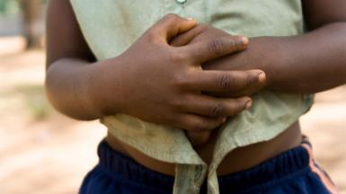 An African girl holds her stomach, symbolising pain or hunger