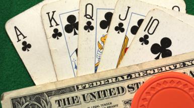 A royal flush in poker - that includes an ace, king, queen, jack and 10 of clubs - are fanned out on a green poker table with a $1 bill and orange chip.