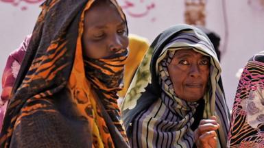 Women in colourful headscarves wait in a queue for food to be distributed.