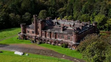 Birds-eye view of a vast Edwardian castle surrounded by trees and greenery.