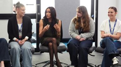 The Duchess of Sussex speaks to young people at a university - they are sit in a semi circle and Meghan is gesturing as she speaks.