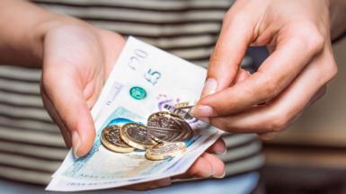 Very close up on a hand holding £5 and £20 note, as well as some one pound coins and a 50 pence piece