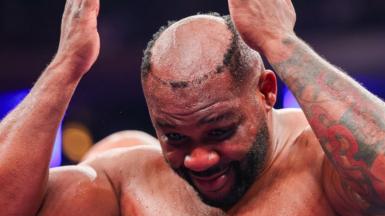 Boxer Jarrell Miller holds his hands to his head as he realises his toupee has fallen off and everyone can see he is bald. His left arm is heavily tattooed.