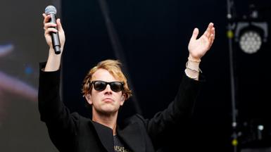 Tom Odell on stage at Radio 1's Big Weekend in 2025, wearing sunglasses and a black jacket