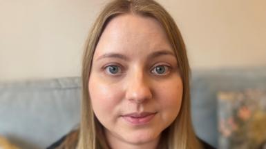 A blonde woman  looks into the camera from her sofa