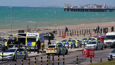 Various police vehicles in a car park on Brighton seafront. Brighton Palace Pier and a choppy sea are in the background