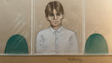 A court sketch of a young man sat in court. He is wearing a white shirt and has medium-length brown hair with a middle parting. 