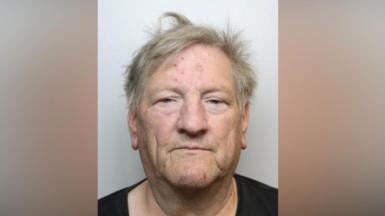 A police mugshot of Christopher Wright. Wright is facing directly toward the camera. He has short, light-coloured hair that appears slightly tousled. Several small red marks are visible on the forehead, and another red mark is visible on the chin. The eyes are partially open, and the face is evenly lit. He is wearing a dark-coloured top, of which only the upper neckline and shoulders are visible.