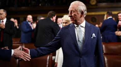 King Charles shakes the hand of a man who cannot be seen off camera as he walks into the chamber