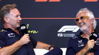 Christian Horner and Flavio Briatore speaking into FIA-branded microphones at a Formula 1 news conference
