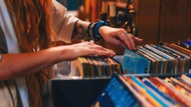 A close up of the arms of a woman flicking through a box of colourful record albums in a record shop