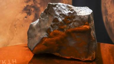 A big lump pf rock glowing solver and red sits on a glass table top.