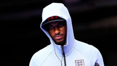 Marcus Rashford wearing a white England zip-up top, hood pulled up over his head