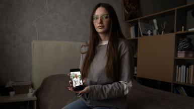 Julia Hripun sitting in her bedroom with a picture of her captive father on her iPhone