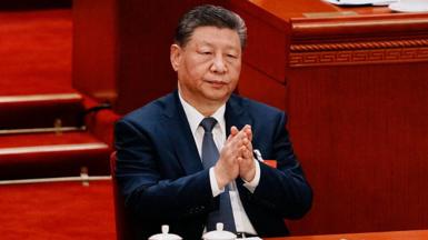 Chinese President Xi Jinping adjusts his navy blue jacket as he sits at the closing session of the Chinese People's Political Consultative Conference (CPPCC) at the Great Hall of the People on March 11, 2026 in Beijing, China. He is sitting in front of a long wooded table with two white tea cups in front of him.