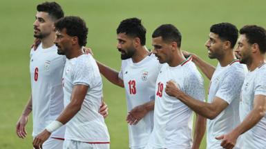Six Iran players, wearing white Iran shirts, stand in a line