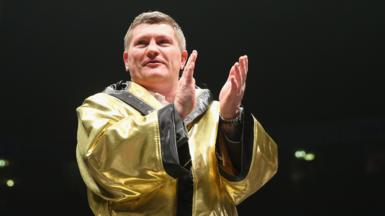 Boxer Ricky Hatton applauds fans while wearing a gold gown in the ring