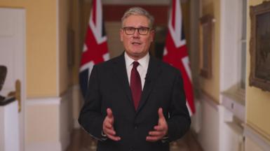 Keir Starmer looks to camera and stands in front of UK flags as he speaks 
