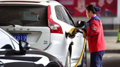 A female petrol station attendant refuels a white car