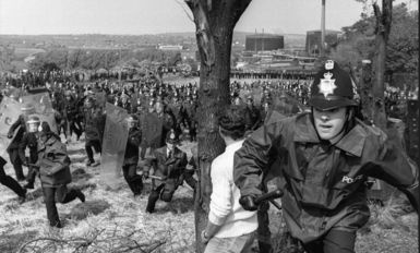 An archive photo of the Orgreave protest from the time. A police officer with a baton can be seen in the foreground with dozens and dozens of other officers dressed in riot gear and with shields in the background